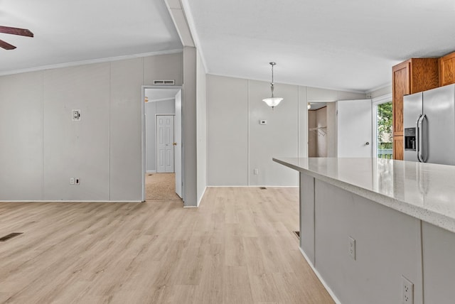 kitchen featuring stainless steel refrigerator with ice dispenser, light stone counters, ornamental molding, light hardwood / wood-style floors, and hanging light fixtures