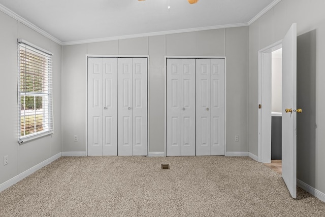 unfurnished bedroom with carpet, crown molding, multiple windows, and multiple closets