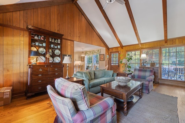 living room with beam ceiling, high vaulted ceiling, wood walls, a chandelier, and light wood-type flooring