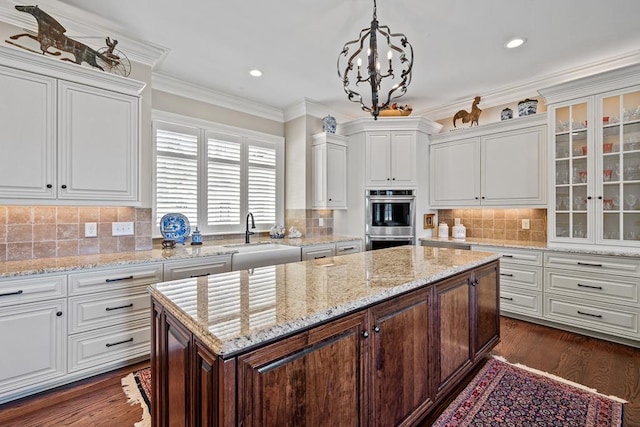kitchen with sink, stainless steel double oven, tasteful backsplash, decorative light fixtures, and white cabinets