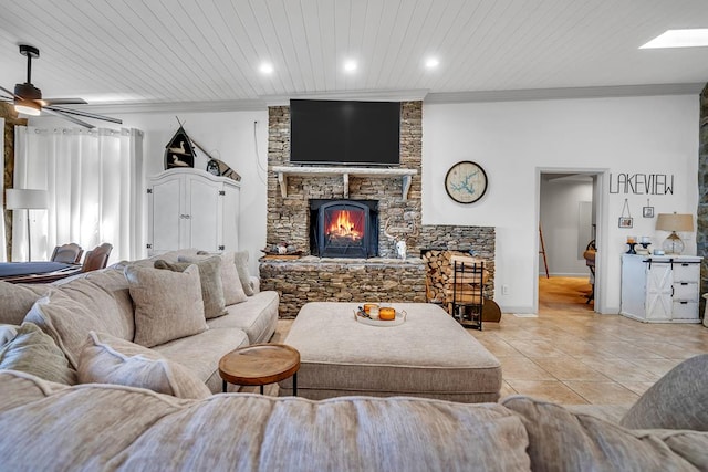 tiled living room with a skylight, ceiling fan, wooden ceiling, a stone fireplace, and crown molding