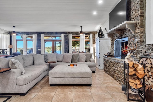 living room featuring ceiling fan, a stone fireplace, and light tile patterned floors