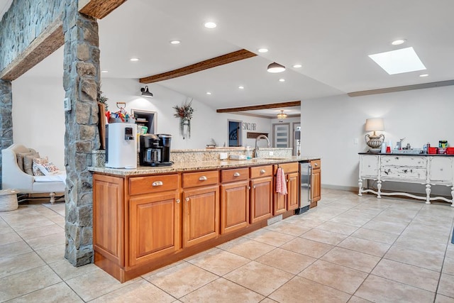 kitchen with a skylight, sink, light stone counters, beamed ceiling, and light tile patterned floors