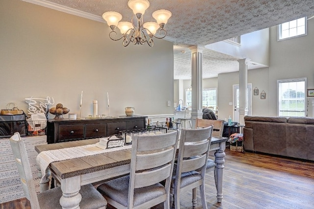 dining room with crown molding, decorative columns, wood finished floors, and a chandelier