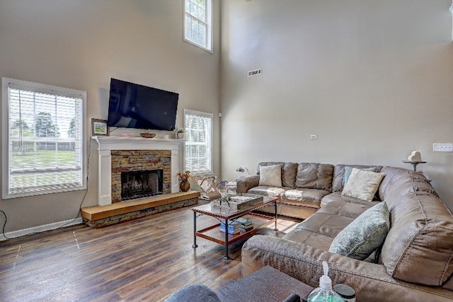 living area featuring visible vents, a towering ceiling, wood finished floors, a fireplace, and baseboards