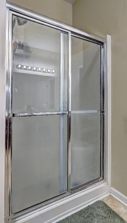 bathroom with baseboards, a shower with shower door, and tile patterned floors