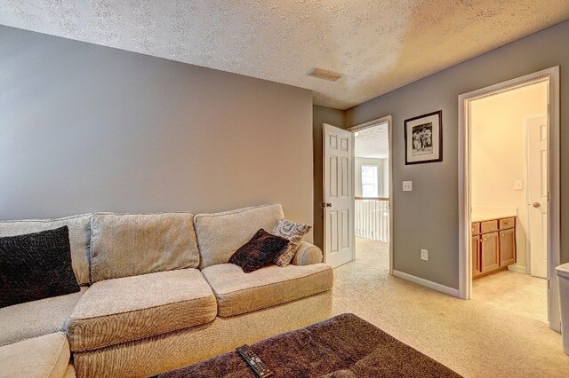 living area with baseboards, light colored carpet, a textured ceiling, and visible vents