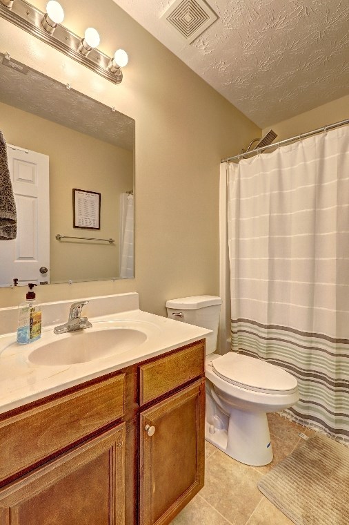 full bath featuring a textured ceiling, visible vents, tile patterned floors, vanity, and toilet