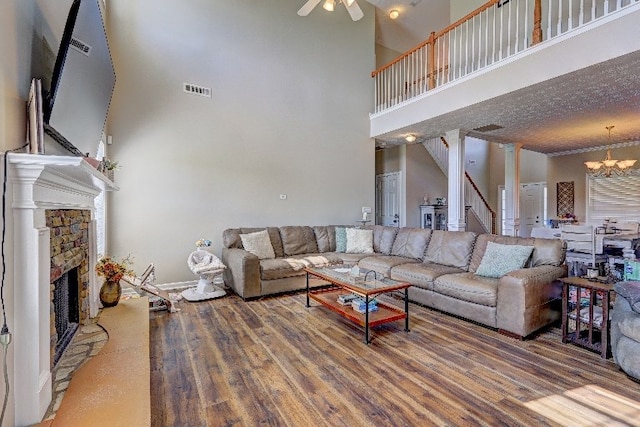 living room featuring visible vents, wood finished floors, a fireplace, a high ceiling, and ceiling fan with notable chandelier