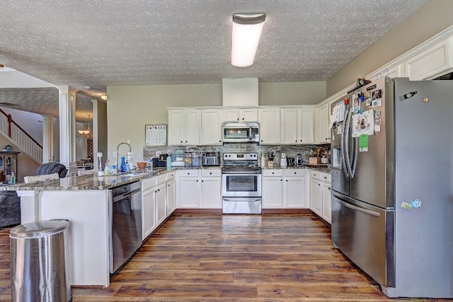 kitchen with decorative columns, dark wood-style flooring, a textured ceiling, a peninsula, and stainless steel appliances