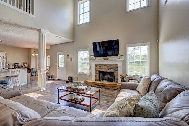 living room featuring decorative columns, a fireplace, wood finished floors, baseboards, and a high ceiling