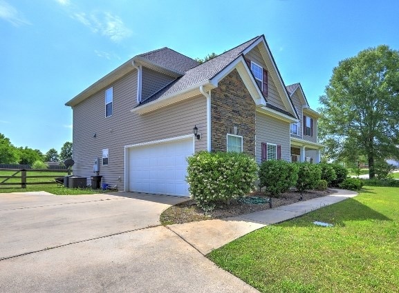 view of home's exterior with driveway, a lawn, fence, an attached garage, and stone siding
