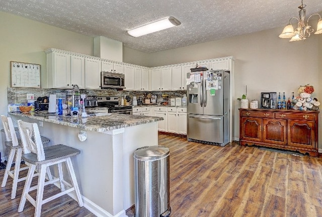 kitchen with a textured ceiling, stainless steel appliances, white cabinetry, a peninsula, and tasteful backsplash
