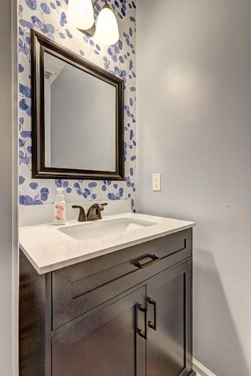 bathroom with vanity, baseboards, and wallpapered walls