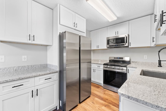 kitchen featuring light stone counters, light wood-style flooring, stainless steel appliances, a sink, and white cabinets