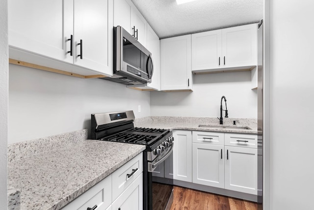 kitchen with stainless steel appliances, white cabinets, a sink, and light stone countertops