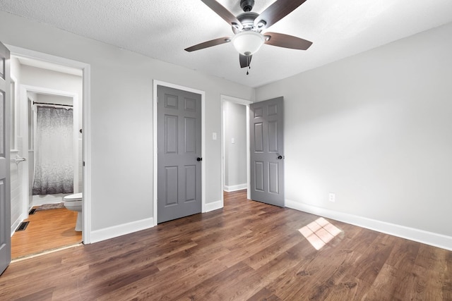 unfurnished bedroom with baseboards, dark wood finished floors, a textured ceiling, and ensuite bathroom