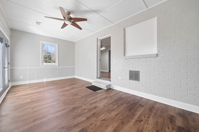 empty room with brick wall, visible vents, and wood finished floors