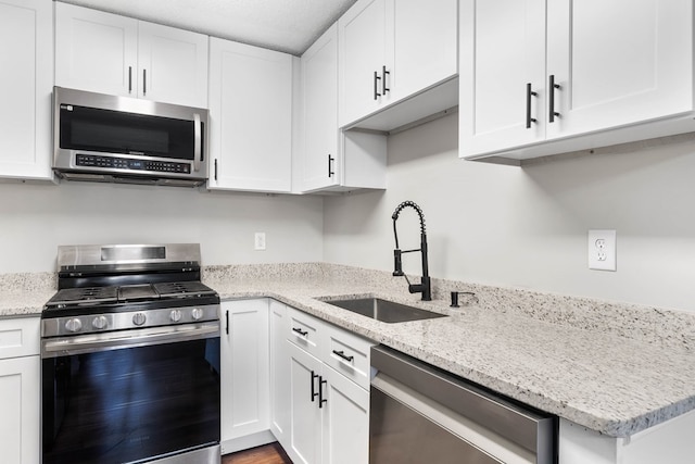 kitchen with light stone counters, appliances with stainless steel finishes, a sink, and white cabinetry