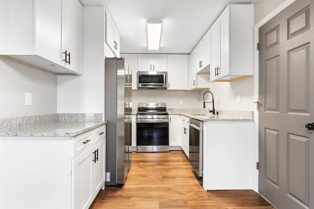 kitchen with appliances with stainless steel finishes, a sink, light wood-style flooring, and white cabinets