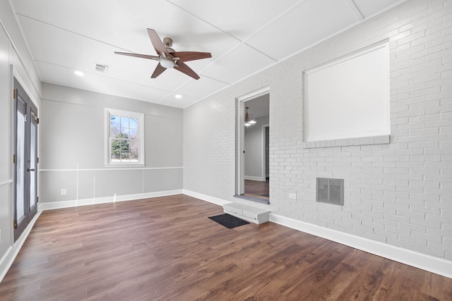 spare room featuring baseboards, visible vents, brick wall, and wood finished floors