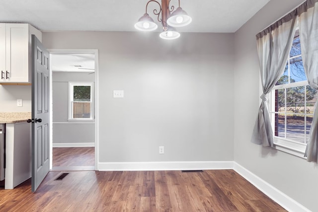 unfurnished dining area with a chandelier, dark wood-type flooring, visible vents, and baseboards