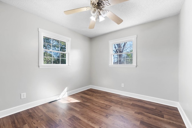 empty room with a textured ceiling, dark wood-type flooring, plenty of natural light, and baseboards