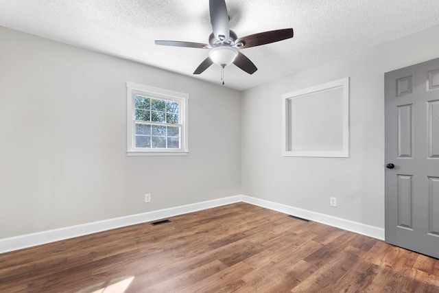 spare room with visible vents, ceiling fan, a textured ceiling, wood finished floors, and baseboards