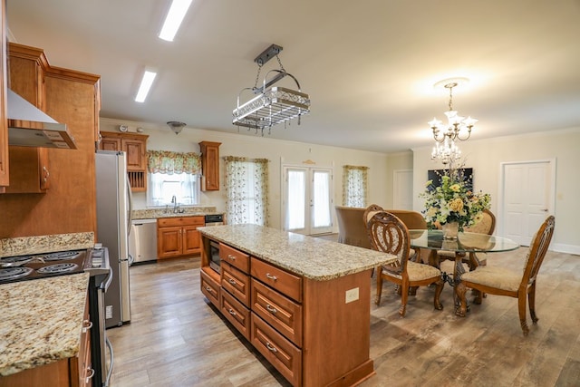 kitchen with light stone countertops, a center island, a notable chandelier, pendant lighting, and appliances with stainless steel finishes