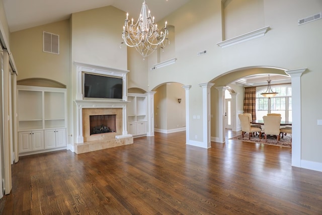 unfurnished living room featuring built in shelves, a premium fireplace, a towering ceiling, and a notable chandelier