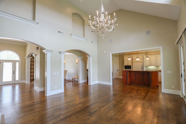 unfurnished living room featuring a notable chandelier, ornate columns, dark wood-type flooring, and a towering ceiling