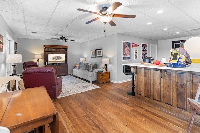 living room with hardwood / wood-style floors, a drop ceiling, and ceiling fan