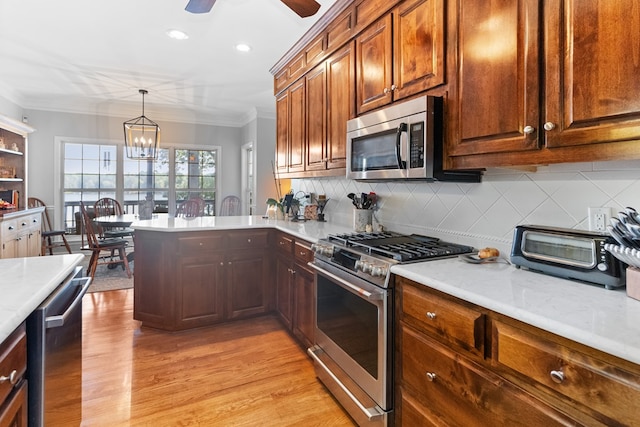 kitchen with hanging light fixtures, ornamental molding, appliances with stainless steel finishes, and light hardwood / wood-style floors