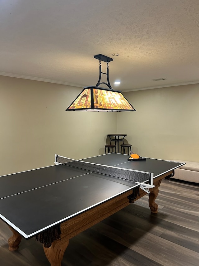 rec room with a textured ceiling, ornamental molding, and dark wood-type flooring