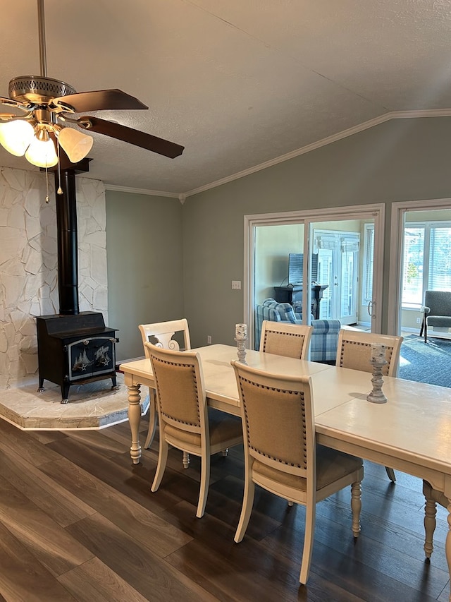 dining area featuring a wood stove, ceiling fan, ornamental molding, vaulted ceiling, and hardwood / wood-style flooring