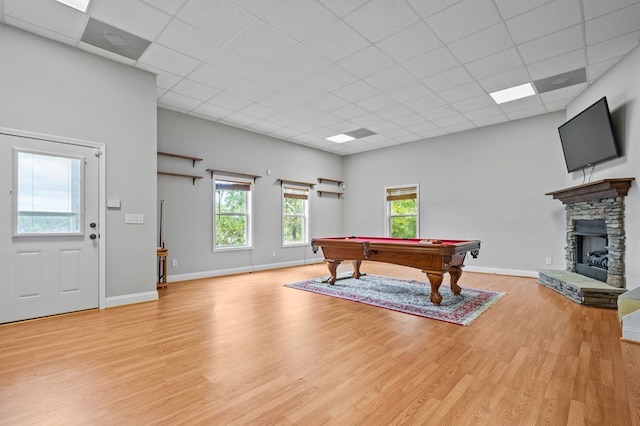 game room with a drop ceiling, a healthy amount of sunlight, light hardwood / wood-style flooring, a stone fireplace, and pool table