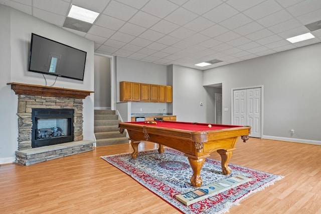 game room featuring light wood-type flooring, a stone fireplace, a drop ceiling, and pool table