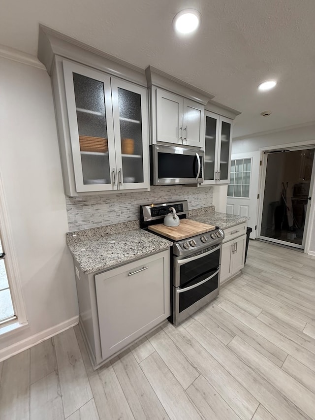 kitchen with decorative backsplash, appliances with stainless steel finishes, light stone countertops, ornamental molding, and light hardwood / wood-style floors