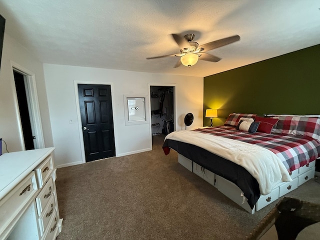 bedroom featuring dark colored carpet, ceiling fan, a spacious closet, a textured ceiling, and a closet