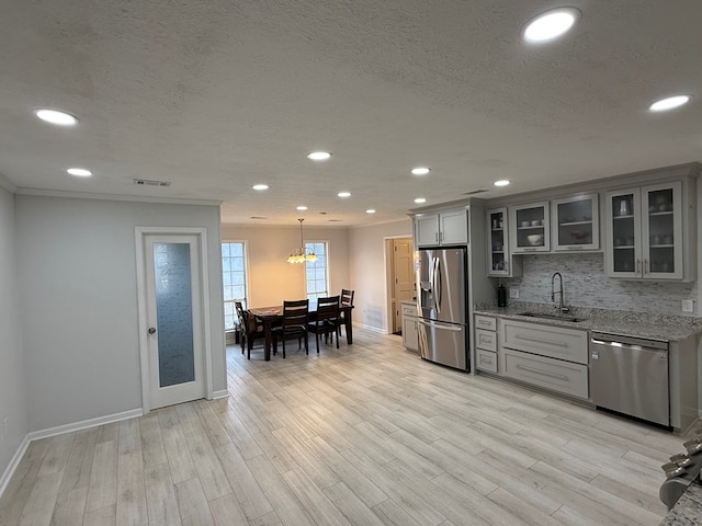 kitchen with light stone counters, stainless steel appliances, sink, pendant lighting, and gray cabinets