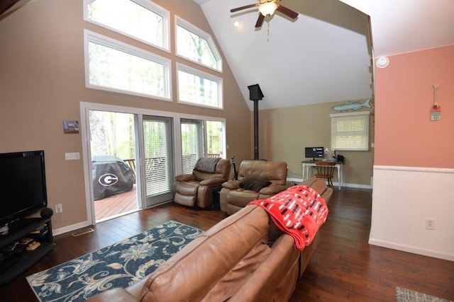 living room featuring baseboards, a ceiling fan, a wood stove, dark wood finished floors, and high vaulted ceiling