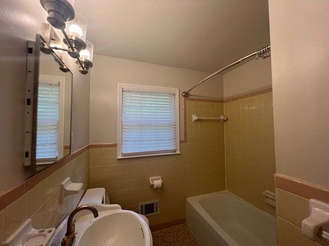 full bathroom featuring tiled shower / bath, sink, tile walls, toilet, and a chandelier