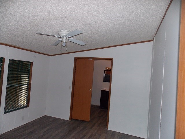 unfurnished room with vaulted ceiling, dark hardwood / wood-style floors, ceiling fan, ornamental molding, and a textured ceiling