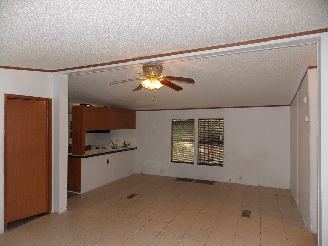 unfurnished living room featuring ceiling fan, sink, ornamental molding, and a textured ceiling