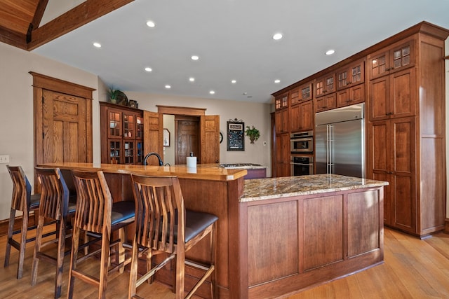 kitchen featuring a large island, stainless steel appliances, light stone counters, light hardwood / wood-style floors, and a breakfast bar area