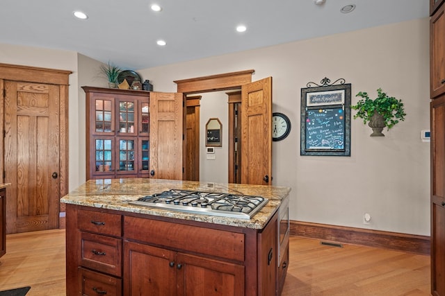 kitchen with a center island, light stone counters, light hardwood / wood-style floors, and stainless steel gas cooktop