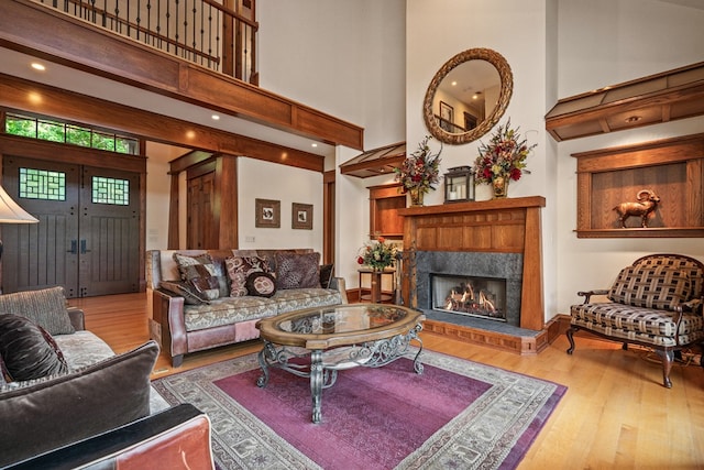 living room with light wood-type flooring, a towering ceiling, and a tiled fireplace