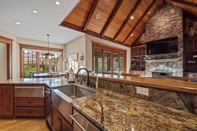 kitchen featuring beamed ceiling, an inviting chandelier, stone countertops, and a stone fireplace