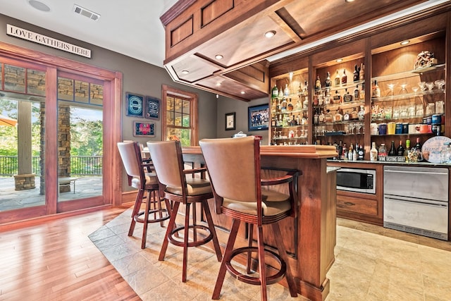 bar featuring stainless steel microwave and light hardwood / wood-style floors