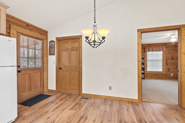 unfurnished dining area with vaulted ceiling, an inviting chandelier, and light hardwood / wood-style floors